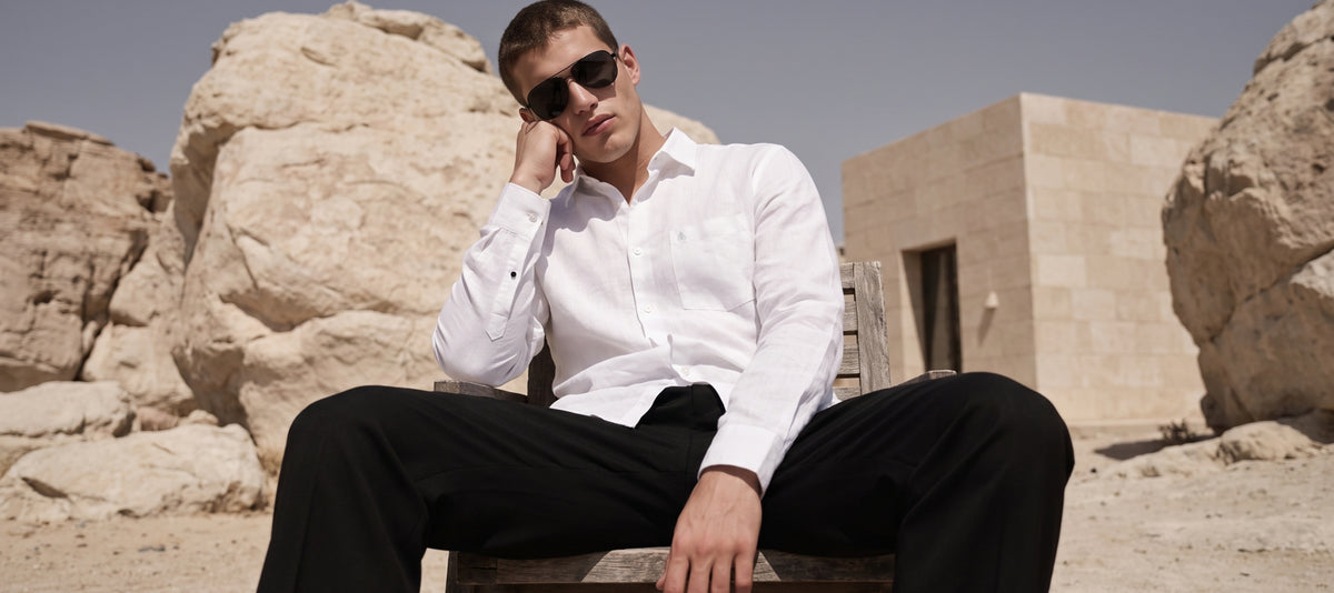 Man in a white linen shirt and black trousers seated among rocks