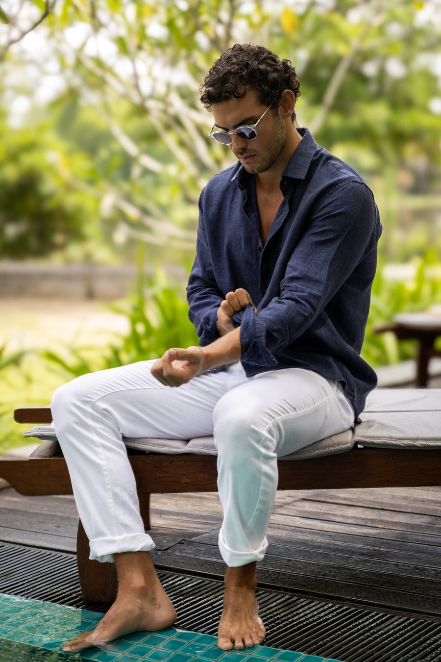 Man in a navy linen shirt seated on a garden daybed