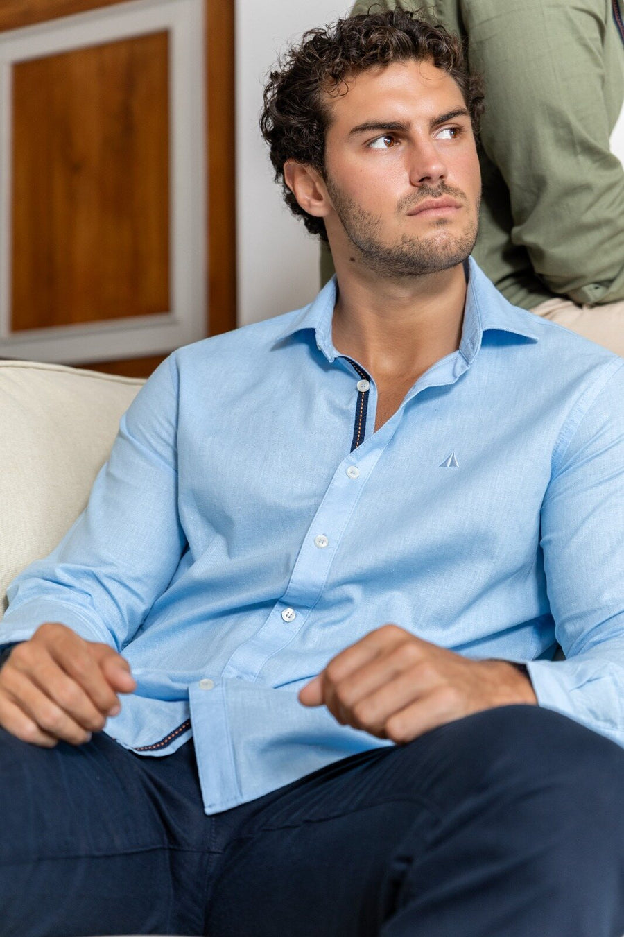 Man in a light blue shirt and navy trousers seated indoors