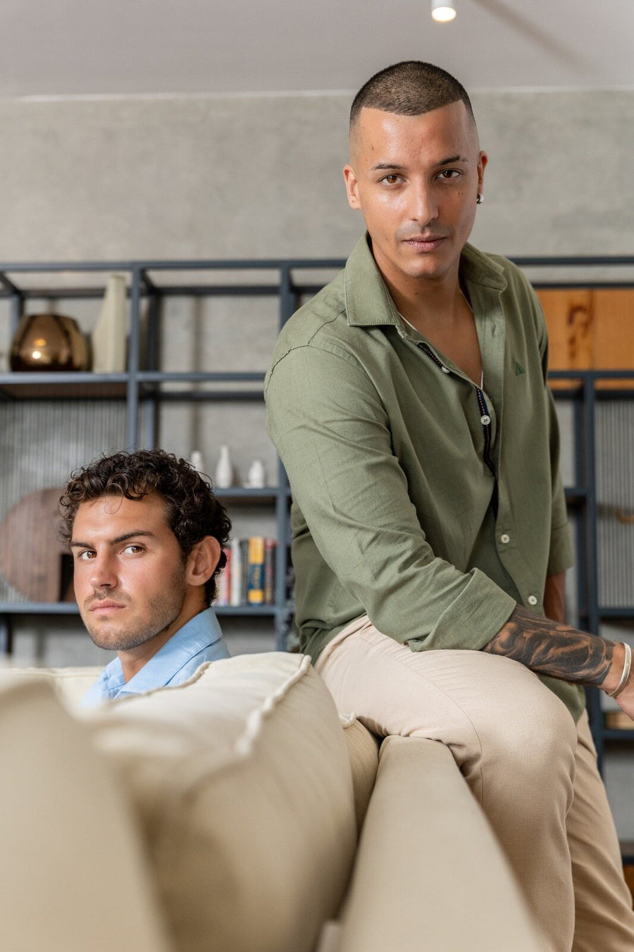 Two men in olive and light blue shirts in a living room